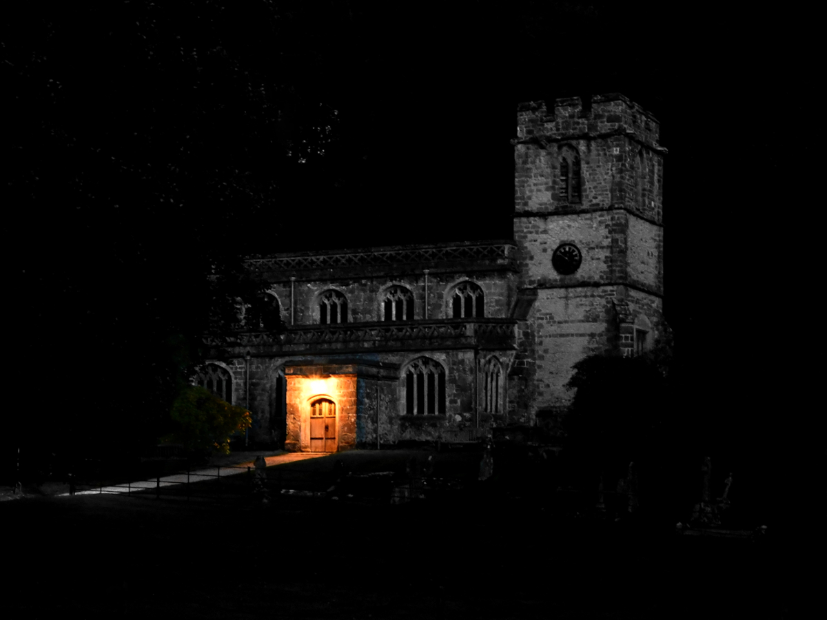 A night photograph of Sourton church with a warm pool of light